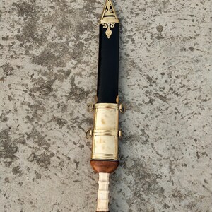 May include: A black and gold Roman Gladius sword with a wooden handle and a decorative pommel. The sword has a leather scabbard with brass accents.