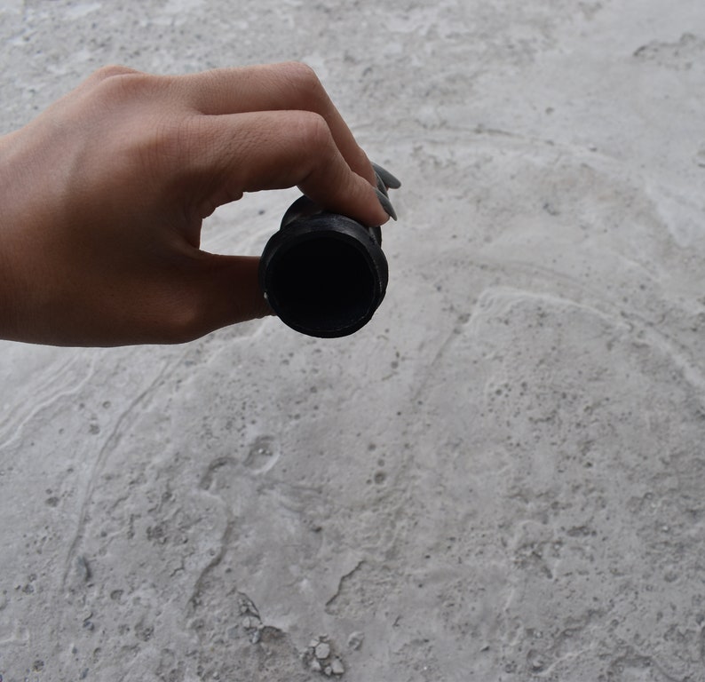 May include: A black rubber drain stopper with a round opening. The stopper is being held by a hand.