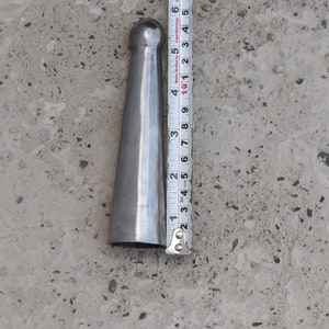 May include: A silver metal tapered rod with a rounded top. The rod is approximately 12.7 cm long and is measured against a ruler.