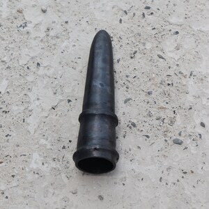 May include: A black rubber nozzle with a pointed tip and a ribbed section. The nozzle is lying on a light gray concrete surface.