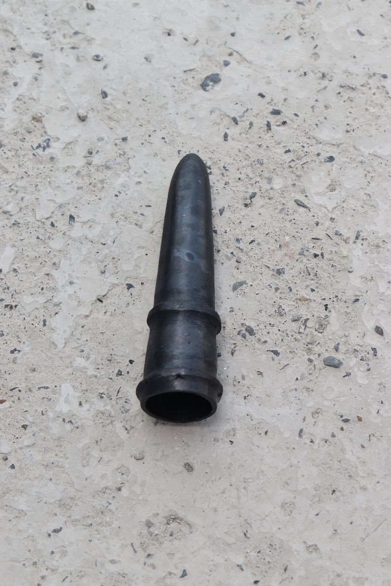 May include: A black rubber nozzle with a pointed tip and a ribbed section. The nozzle is lying on a light gray concrete surface.