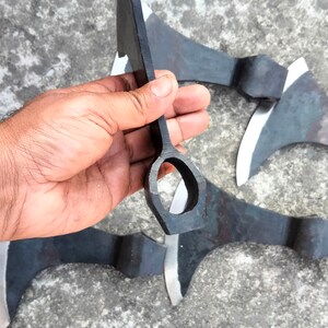 May include: Four black metal hand axes with a hole in the handle. The axes are on a gray concrete surface.