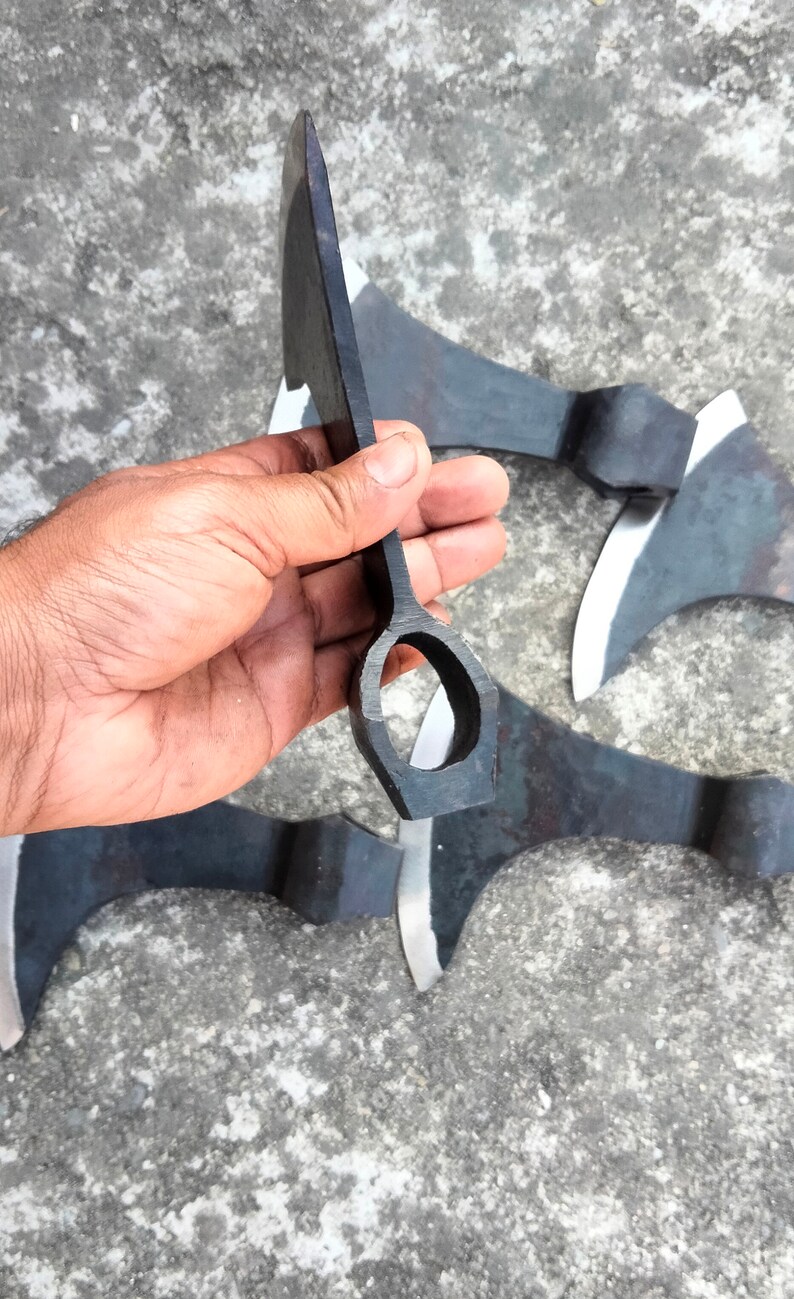 May include: Four black metal hand axes with a hole in the handle. The axes are on a gray concrete surface.