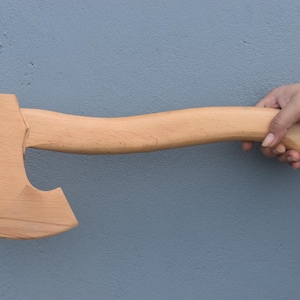 Könnte beinhalten: Eine Axt aus Holz mit einem gebogenen Stiel. Die Axt ist aus hellem Holz und hat eine natürliche Oberfläche.