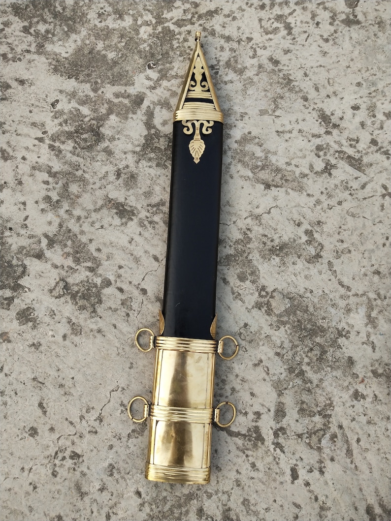 May include: A black scabbard with gold accents and a decorative top. The scabbard has two rings on each side.
