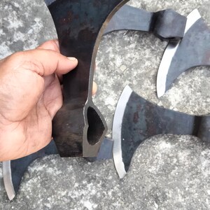 May include: A set of four black hand-forged axes with a hole in the handle. The axes are on a gray concrete surface.