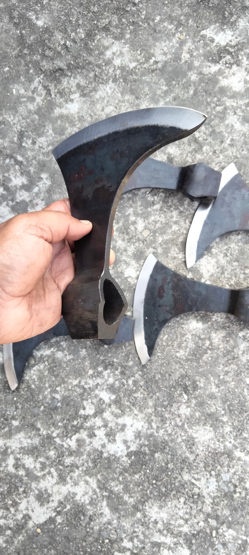 May include: A set of four black hand-forged axes with a hole in the handle. The axes are on a gray concrete surface.