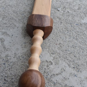 K&ouml;nnte beinhalten: Ein Holzschwert mit einem braunen Griff und einer hellbraunen Klinge. Der Griff hat einen runden Knopf am Ende und ein gedrehtes Design in der Mitte.