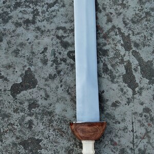 May include: A silver sword with a wooden handle. The handle has a white, textured grip and a brown, rounded pommel.