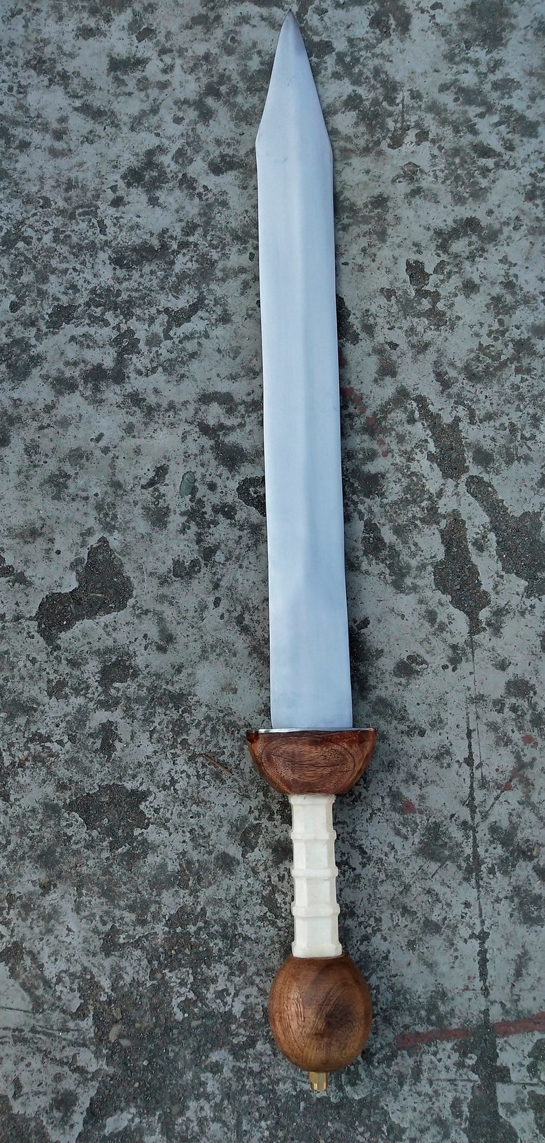 May include: A silver sword with a wooden handle. The handle has a white, textured grip and a brown, rounded pommel.
