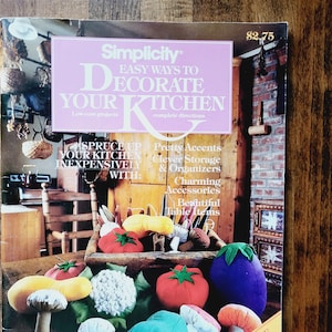 May include: A Simplicity magazine cover featuring a colorful collection of felt food items, including a tomato, eggplant, mushroom, and cauliflower. The magazine cover text reads "Easy Ways to Decorate Your Kitchen" and "Many Full-Size Patterns".