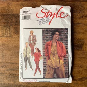 May include: A white paper sewing pattern envelope labelled Style 1853. The front features illustrations of various outfits including blazers, tops, and trousers, alongside a photograph of a person wearing a rust-coloured blazer over a gold top.