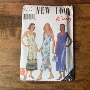 May include: A vintage New Look sewing pattern showing illustrations of three long dresses. The pattern includes a floral print dress, a light blue dress with a slit, and a solid purple dress. The pattern is labelled "Easy" and goes up to size 22.