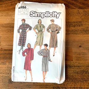 May include: Simplicity sewing pattern number 6986 for a dress. The pattern shows four different styles of dresses, all with long sleeves and button-up fronts. The dresses are in various colours and patterns, including plaid, solid, and striped.