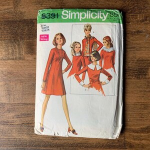 May include: Vintage Simplicity sewing pattern packet. The packet features illustrations of women's dresses and outfits in shades of orange and red. The packet has the number 8391 and the word "Simplicity" in green and white.