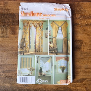 May include: A Simplicity 5050 ShowHouse Windows sewing pattern envelope featuring illustrations of various window treatments including floor-length curtains with valances and roman shades in yellow and blue floral and striped fabric patterns.