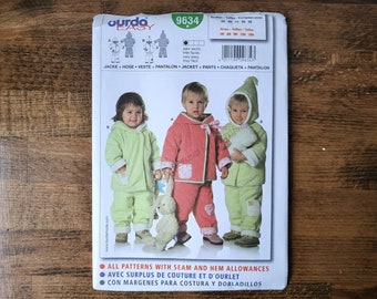 May include: A sewing pattern for children's jackets, pants, and vests. The pattern features three children wearing different colored outfits. The pattern includes the text "9634" and "ourda EASY". The outfits are in shades of pink and green.