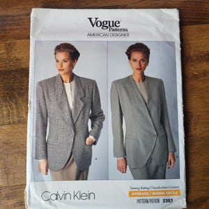 May include: A sewing pattern for a blazer by Calvin Klein. The pattern features two different styles of blazers, one with a plaid pattern and the other with a solid colour. The pattern is labelled "Vogue Patterns American Designer" and "Pattern/Patron 2393".
