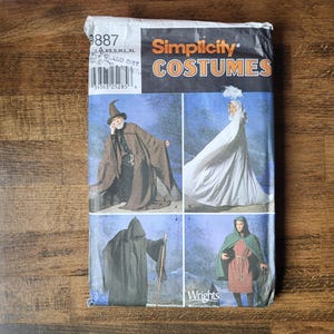 May include: A Simplicity Costumes sewing pattern envelope, number 9887, featuring illustrations of four different hooded cloaks and robes. The package displays a wizard in a brown cloak, a figure in a white cape, a dark hooded robe, and a green cloak.