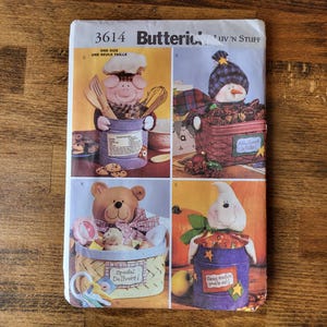 May include: A sewing pattern for four different stuffed toy containers. The containers are shaped like a pig, snowman, teddy bear, and ghost. Each container has a different design and features a cute face. The pattern is titled "Butterick's Luv N Stuff" and includes the number "3614".