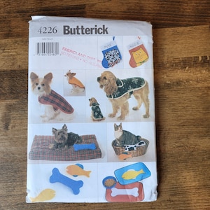 May include: A sewing pattern for making dog clothes and accessories. The pattern is for sizes XS to XL and includes instructions for making a plaid dog coat, a snowflake dog coat, a dog bed, and a dog toy. The pattern is from Butterick and has the number 4226 on it.
