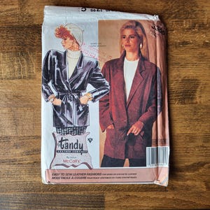 May include: A sewing pattern for two jackets, one black and one brown, with the text "Tandy by pour McCall's" and "Easy to sew leather fashions for dress or synthetic leather. Mode facile a coudre pour peaux vestibles ou cuirs synthetiques."