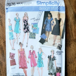 Peut inclure: Pochette de patron de couture Simplicity design studio avec des illustrations de robes. Le paquet comprend des informations de taille et le texte "simple graphics". Le paquet est sur une surface en bois.