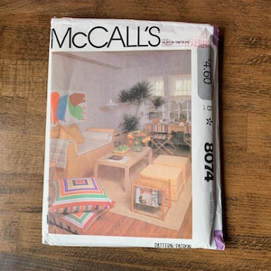 May include: A McCall's sewing pattern envelope, number 8074, featuring a printed photograph of a living room interior with a sofa, coffee table, and colorful square floor cushions. The white paper envelope includes the brand name and pattern number.
