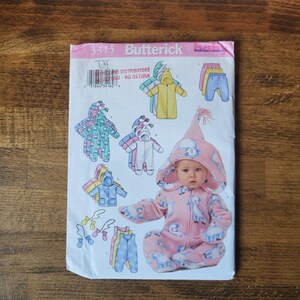 May include: A sewing pattern for a baby's hooded jumpsuit with a unicorn design. The pattern is from Butterick and is number 3315. The pattern includes instructions for making a hooded jumpsuit, trousers, and a hat.