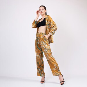 May include: A woman wearing a black bra and a gold satin shirt and pants with a floral print. The shirt has a collar and long sleeves. The pants have a wide leg.