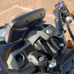 以下が含まれることがあります： 黒いオートバイのハンドルバーマウントに、黒と銀のGPSデバイスが取り付けられています。マウントにはクイックリリースレバーと銀色のネジが付いています。
