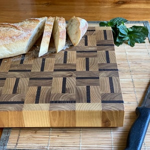 Può includere: Un tagliere di legno con un motivo a scacchi di legno chiaro e scuro. Una pagnotta di pane è tagliata sul tagliere, e un coltello è sul tavolo accanto.