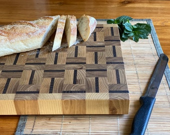 May include: A wooden chopping board with a chequered pattern of light and dark wood. A loaf of bread is sliced on the board, and a knife is on the table next to it.