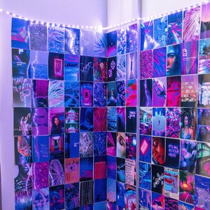 May include: A wall covered in a collage of colorful, abstract, and graphic images. The images are arranged in a grid pattern and feature a variety of colors, including blue, purple, pink, and white. The wall is lit by a string of white lights. The wall is in a bedroom with a pink and gray pillow on a bed.
