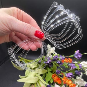 May include: A set of clear plastic butterfly wing shapes, stacked and held in a hand. The wings are designed for crafting and are approximately 3 inches wide.