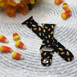 May include: Black Apple Watch band with a candy corn pattern. The band is made of silicone and has a black background with yellow and orange candy corn printed on it.