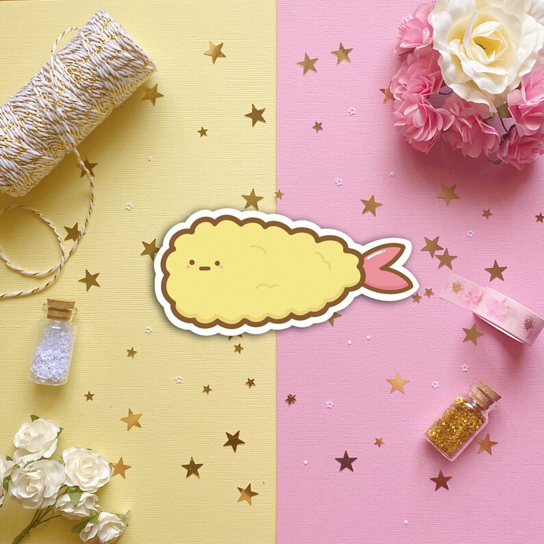 May include: A yellow cartoon shrimp tempura with a pink tail, surrounded by gold stars on a yellow and pink background.