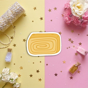 May include: A yellow and white cartoon illustration of a rolled cake on a pink and yellow background with gold stars.