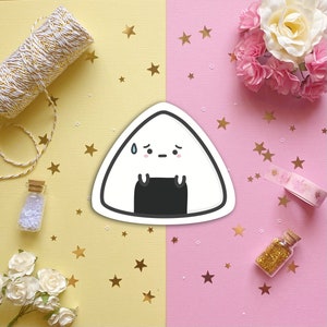 May include: A white and black cartoon onigiri with a sweat drop on its forehead and a sad expression. The onigiri is surrounded by gold stars on a yellow background and pink stars on a pink background.