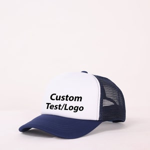 Könnte beinhalten: Eine weiße und marineblaue Trucker-Kappe mit Netzrücken. Die Vorderseite der Kappe trägt den Text "Custom Test/Logo" in Schwarz.