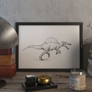 May include: A black and white drawing of a Spinosaurus dinosaur in a black frame on a wooden table with a lamp, a candle, a stack of books, and a decorative object.