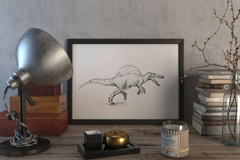 May include: A black and white drawing of a Spinosaurus dinosaur in a black frame on a wooden table with a lamp, a candle, a stack of books, and a decorative object.