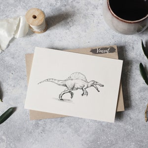 May include: A black and white drawing of a Spinosaurus dinosaur on a white card with the name "Vincent" written in black on a brown background.