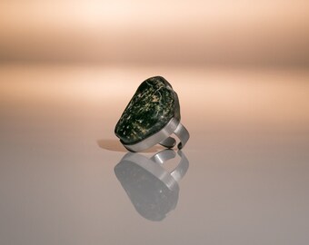 Puede incluir: Un anillo de piedra verde con una banda de plata. La piedra tiene una forma irregular y una textura rugosa.
