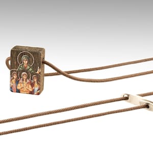 Op de afbeelding: Een bruine houten hanger met een kleurrijk beeld van een religieuze figuur en andere mensen. De hanger is bevestigd aan een bruin koord met een zilveren sluiting.