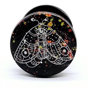 May include: Black ear gauge with a white moth design and orange and yellow glitter accents.