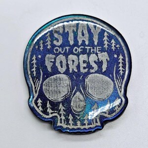 May include: A blue and silver skull with the text "STAY OUT OF THE FOREST" printed on it. The skull is surrounded by a forest design.