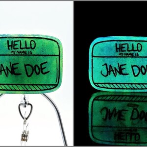 May include: A green and blue name tag with black text that reads "HELLO MY NAME IS JANE DOE". The name tag is made of glass and glows in the dark.