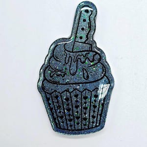 May include: A silver glitter cupcake with a black outline and a knife sticking out of the top. The knife is also outlined in black and has a silver glitter handle.