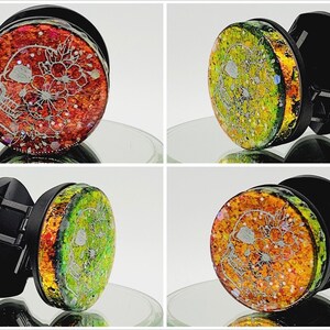 May include: A black phone grip with a round, colourful, glittery skull design. The skull is white with floral details and is surrounded by red, orange, yellow and green glitter.